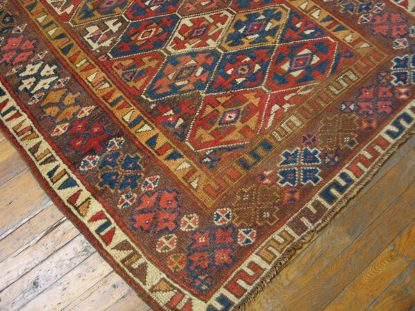 Low pile rug with complex red, blue, and gold geometric patterns rests on wood planks.