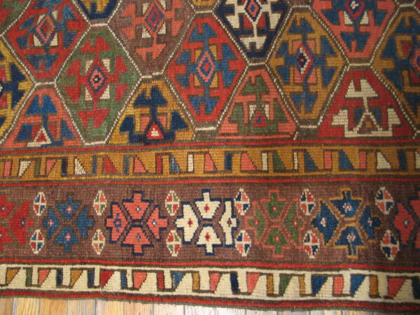 Detail of a complex geometric rug featuring colorful hexagons and multiple striped borders over wood planks.