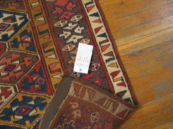 A folded rug with geometric patterns in red, navy, brown, and tan sits on honey-toned wood flooring.