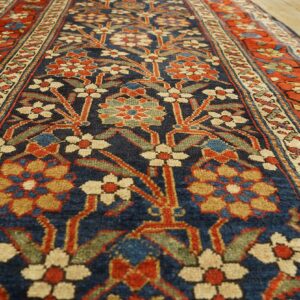 A patterned runner rug featuring navy, red, and cream stylized floral designs on wood plank flooring.