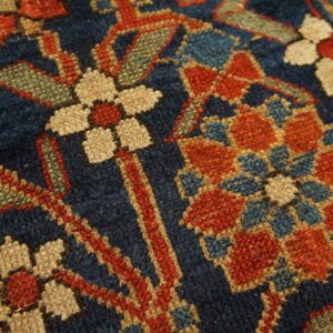 Rustic low-pile rug texture with navy, brick red, tan, and green geometric floral patterns.