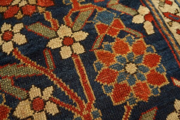 Rustic low-pile rug texture with navy, brick red, tan, and green geometric floral patterns.