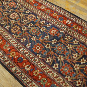 Long runner featuring a complex floral pattern on a navy field and multiple rust red borders over wood floor.