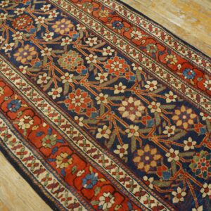 Navy, red, and light floral runner with multiple borders rests on aged wooden floorboards.