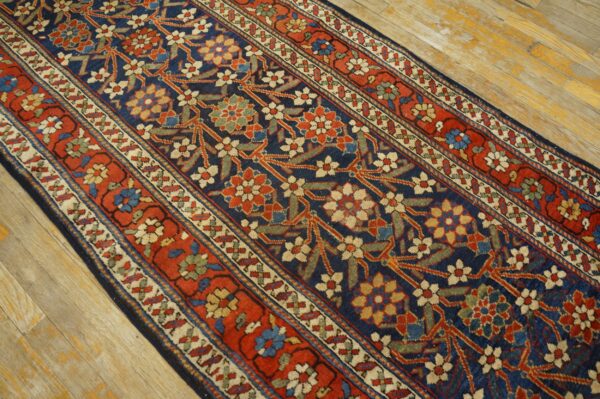 Navy, red, and light floral runner with multiple borders rests on aged wooden floorboards.