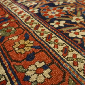 Detailed view of a traditional rug pattern featuring red borders, a navy field, and cream floral motifs.