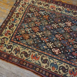 Low-pile rug with dark geometric field and blue, rust, and cream borders on distressed wood floors.