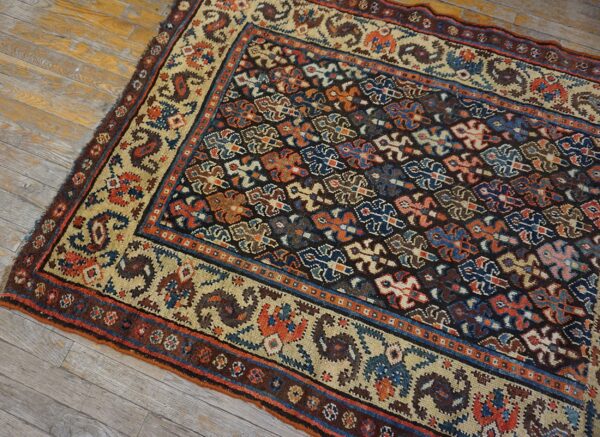 Low-pile rug with dark geometric field and blue, rust, and cream borders on distressed wood floors.