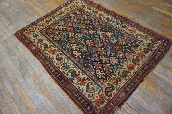 Multi-colored geometric rug with a dark field and tan border on distressed gray wooden plank flooring.
