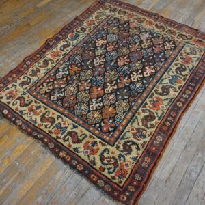 Multicolor geometric rug with a dark field and cream border lies on distressed wide-plank wooden floor.