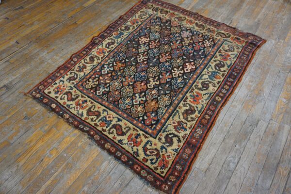 Multicolor geometric rug with a dark field and cream border lies on distressed wide-plank wooden floor.