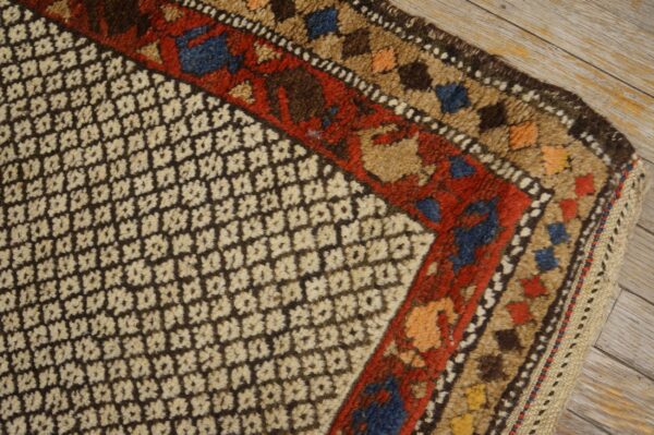High-pile rug corner showing a dark brown geometric field and multi-colored borders on light wood flooring.