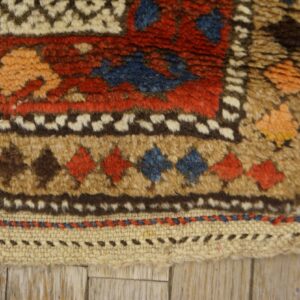 Shaggy rug detail showing geometric motifs and a flat woven edge on light wood planks.