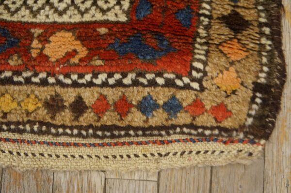 Shaggy rug detail showing geometric motifs and a flat woven edge on light wood planks.