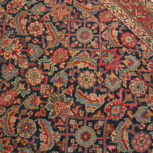 Detailed navy rug with red, gold, and light blue floral patterns, showing a red border on wood floor.