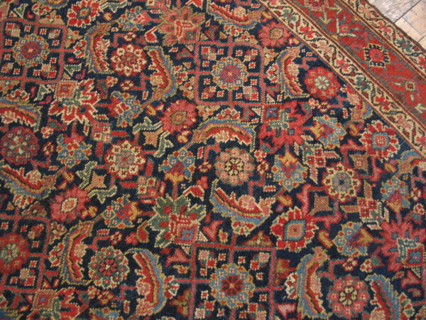 Detailed navy rug with red, gold, and light blue floral patterns, showing a red border on wood floor.