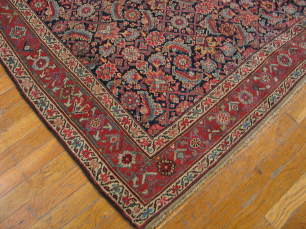 Detail of a traditional navy and red patterned rug with a wide border on distressed hardwood floors.