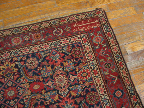 Ornate red and navy traditional rug with detailed patterns and visible script rests on distressed wooden floorboards.