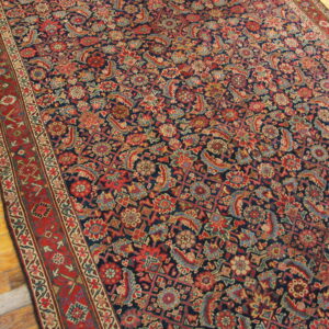 Navy blue rug featuring intricate traditional red and blue floral patterns on light wooden plank flooring.