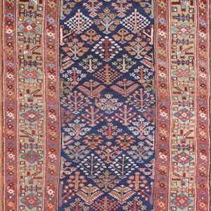 Low-pile runner rug featuring dense geometric tree patterns on a navy blue field with rust and tan borders.