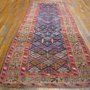 Narrow tribal runner rug with a navy geometric center, red borders, and green accents on wood flooring.