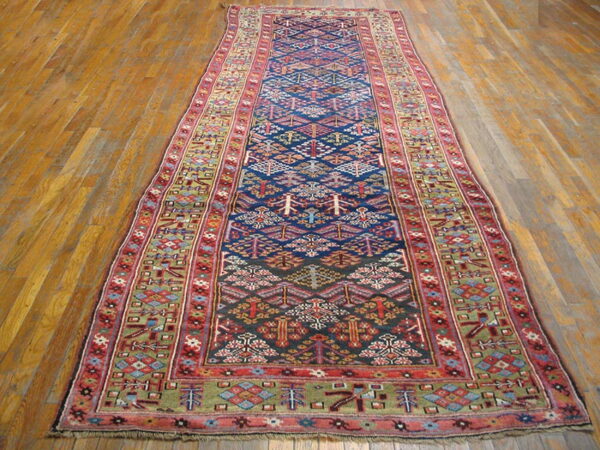 Narrow tribal runner rug with a navy geometric center, red borders, and green accents on wood flooring.