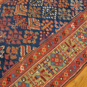Low-pile rug with geometric patterns in deep blue, red, and green borders, placed on glossy wood flooring.
