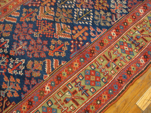 Low-pile rug with geometric patterns in deep blue, red, and green borders, placed on glossy wood flooring.