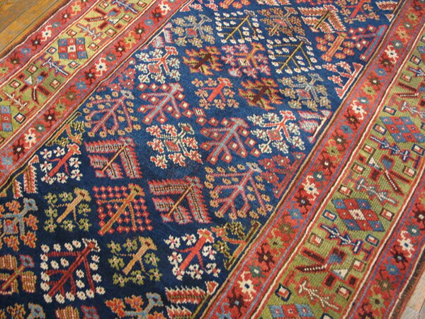 Blue rug runner with repeating red and tan tribal patterns, thick green and red borders, resting on wood flooring.