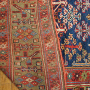 Geometric green and red flatweave pattern contrasts a high-pile blue rug design on hardwood floor.