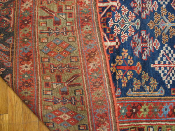 Geometric green and red flatweave pattern contrasts a high-pile blue rug design on hardwood floor.