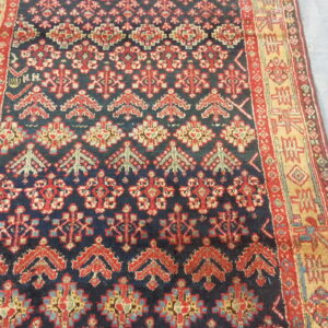 Navy rug with repeating red, yellow, and blue geometric motifs and thick patterned borders on a light surface.