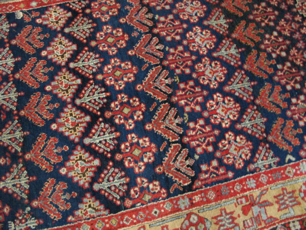 Navy blue rug featuring a tight pattern of red, light blue, and beige stylized geometric motifs and borders.