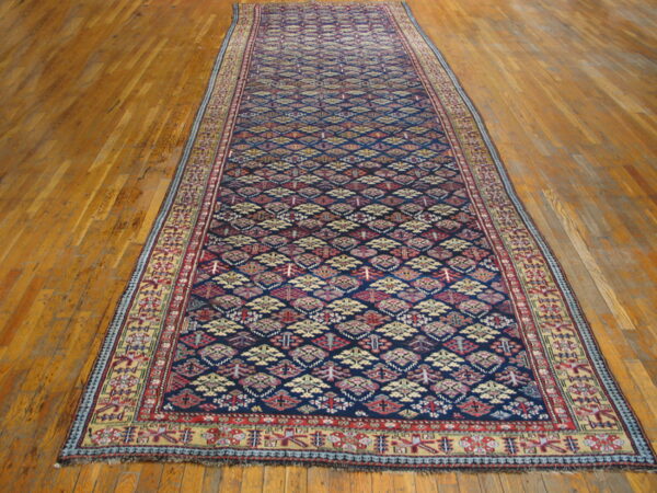Dark blue runner rug featuring red, cream, and yellow diamond motifs on wooden flooring.