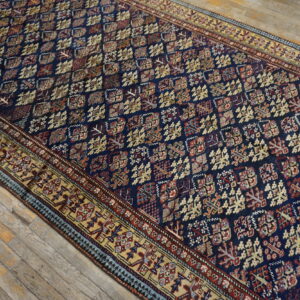 Navy blue rug with a dense geometric pattern and wide beige border rests on distressed wood flooring.