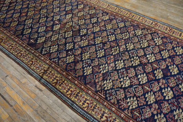 Navy blue rug with a dense geometric pattern and wide beige border rests on distressed wood flooring.