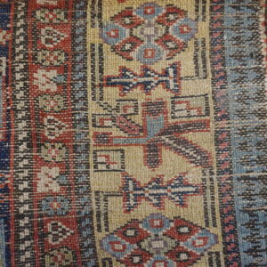 Close-up of low-pile beige, red, and blue geometric patterning adjacent to dark navy high pile rug.