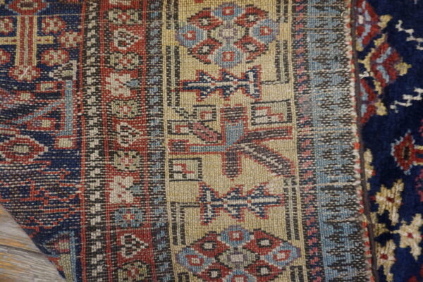 Close-up of low-pile beige, red, and blue geometric patterning adjacent to dark navy high pile rug.