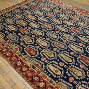 Traditional navy rug with repeating multicolor boteh designs and a complex red border on wood floors.