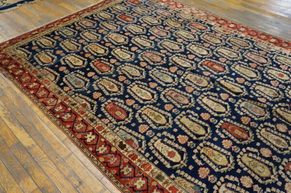 Traditional navy rug with repeating multicolor boteh designs and a complex red border on wood floors.