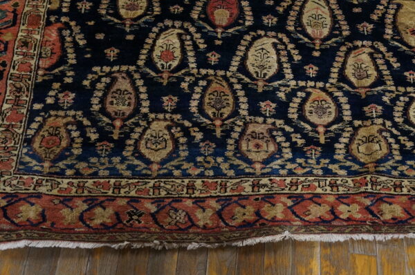 Navy blue rug with distressed tan and red paisley patterns and complex borders over light wood planks.