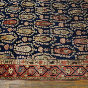 Navy rug featuring stylized boteh shapes and a rust geometric border on a distressed wooden floor.