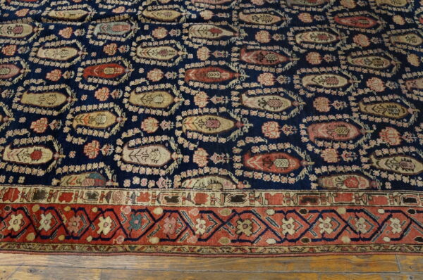Navy rug featuring stylized boteh shapes and a rust geometric border on a distressed wooden floor.