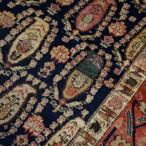 Detailed view of a dark blue rug with repeating cream and pink paisley motifs and a rust-red border.