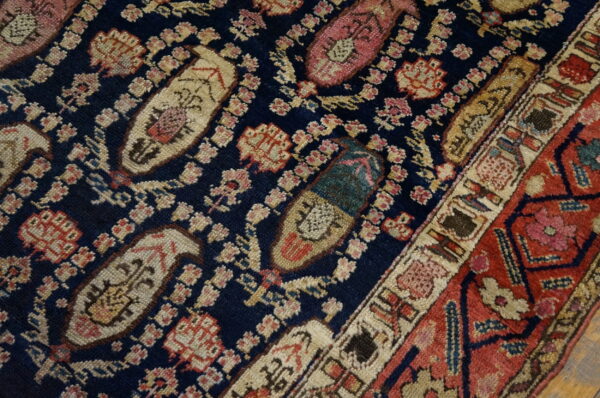 Detailed view of a dark blue rug with repeating cream and pink paisley motifs and a rust-red border.