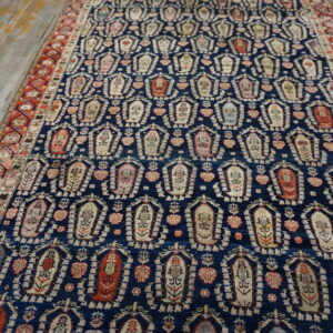 Navy rug patterned with repeating light floral motifs and a rust red border lies on distressed wood flooring.