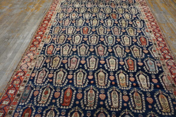 Navy rug patterned with repeating light floral motifs and a rust red border lies on distressed wood flooring.