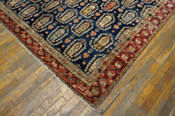 Blue rug corner featuring ogee motifs and a geometric red border resting on distressed, weathered hardwood flooring.