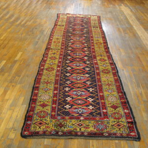 Colorful geometric runner rug with red, blue, and gold motifs laid on light wood floorboards.