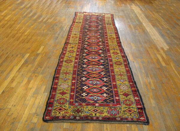 Colorful geometric runner rug with red, blue, and gold motifs laid on light wood floorboards.